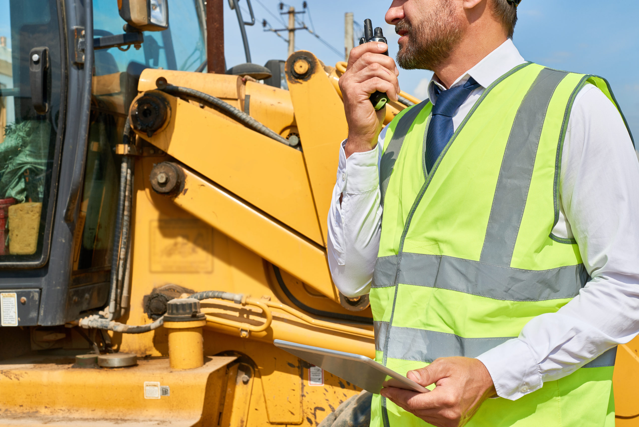 Construction Foreman uses a radio to effectively communicate with his team, while maintaining Social Distance Guidelines